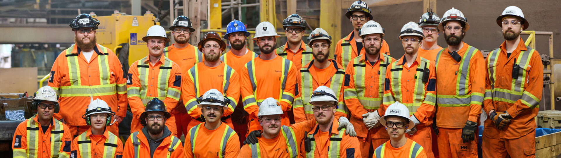 Group of men in orange protective jumpsuits posing in front of a grinding mill