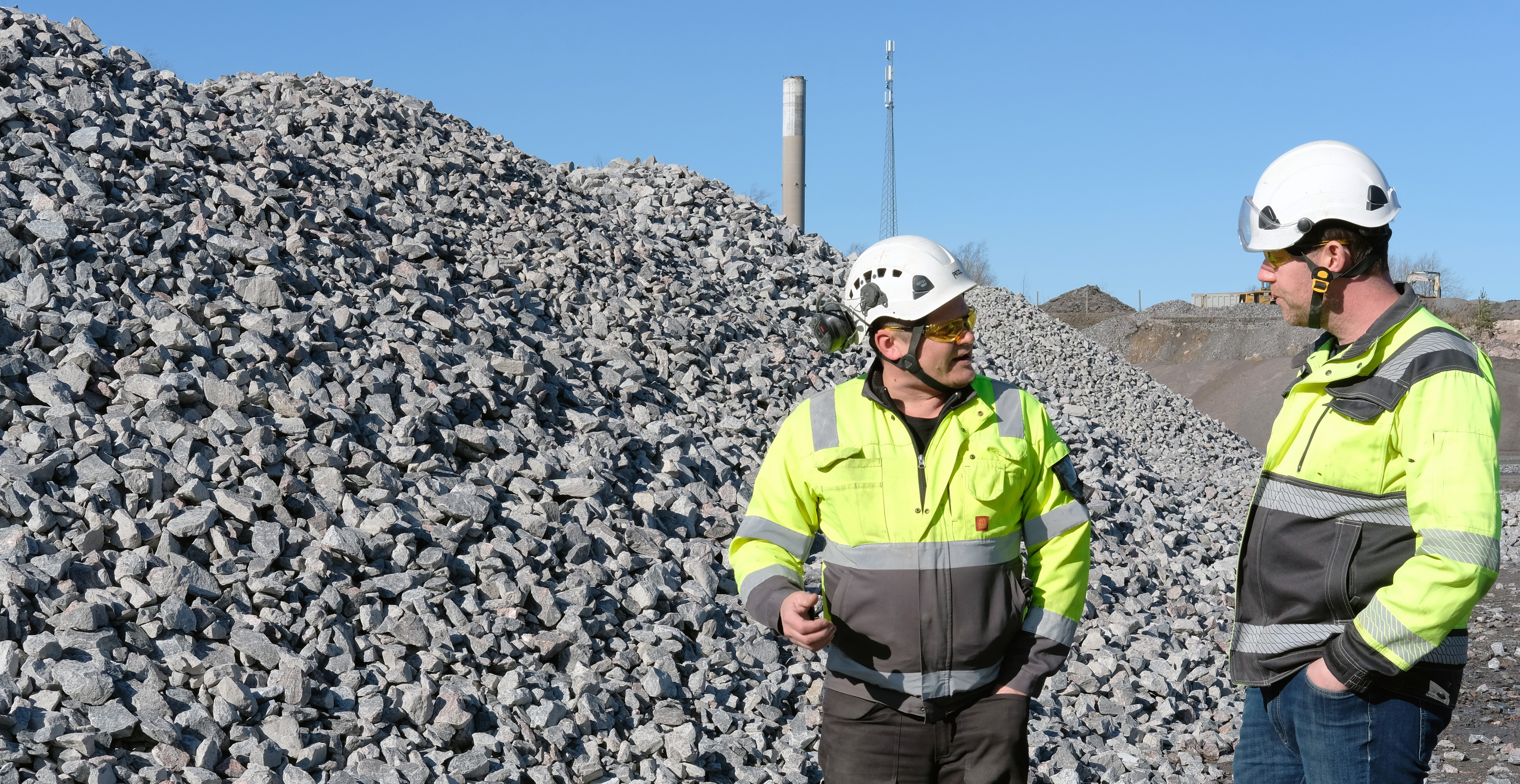 Two people standing in front of piles of aggregate. 