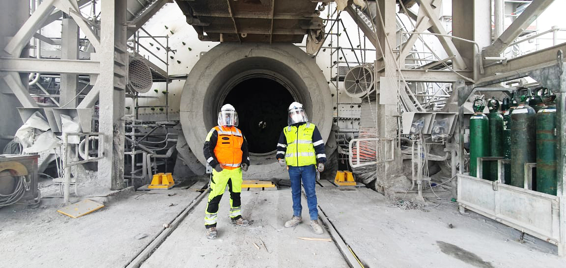 Two men in front of ball mill opening.