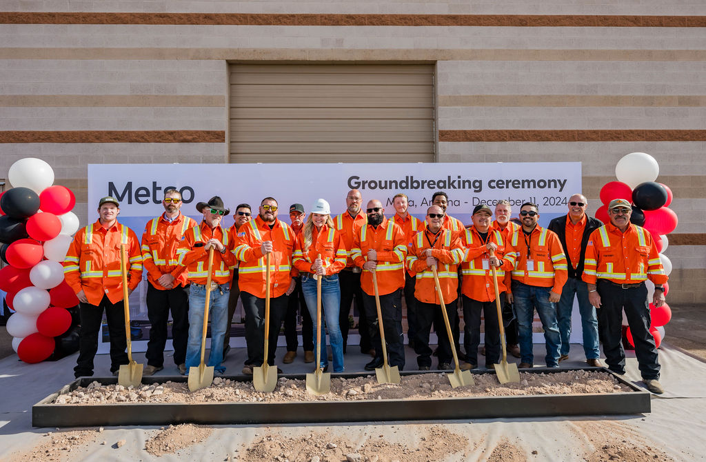 Un grupo de personas vestidas con EPI naranja sosteniendo palas y de pie frente a un telón de fondo en la ceremonia de inauguración de Metso.