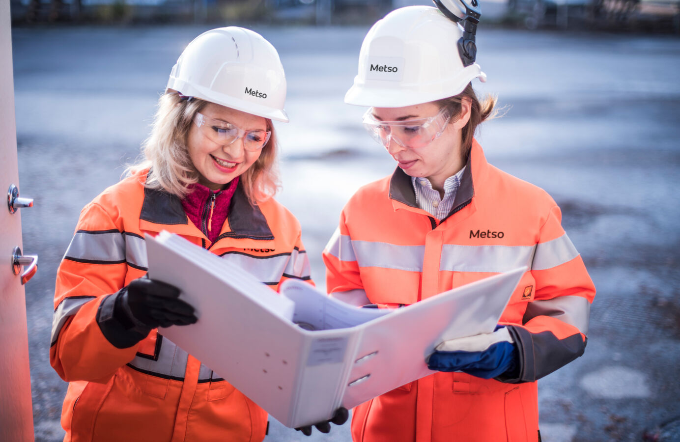 Two women with work gear looking at folder in their hands.