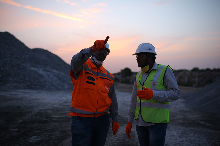 Two men in a sunset at a quarry facing the camera and the other pointing forward.
